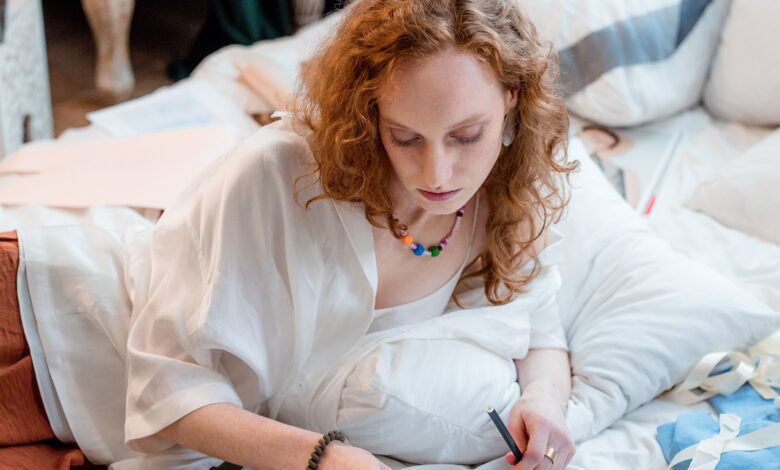 Fashion designer working at a studio desk with sketches, fabric swatches, measuring tools, and clothing samples.