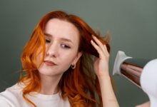 Woman styling her hair at home with a round brush and hair dryer to create a smooth, bouncy blowout.