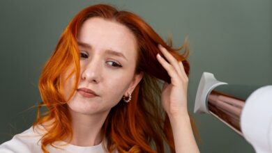 Woman styling her hair at home with a round brush and hair dryer to create a smooth, bouncy blowout.