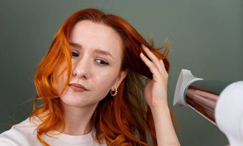 Woman styling her hair at home with a round brush and hair dryer to create a smooth, bouncy blowout.