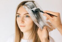 A person applying hand-painted highlights to sections of hair at home to create a soft balayage effect.